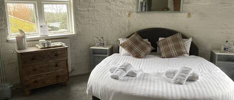 A bedroom with a large bed, a wooden dresser, a window, and a mirror on the wall.