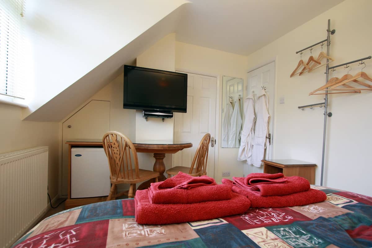 A bedroom with a bed, a desk, a chair, a television, and a drying rack.