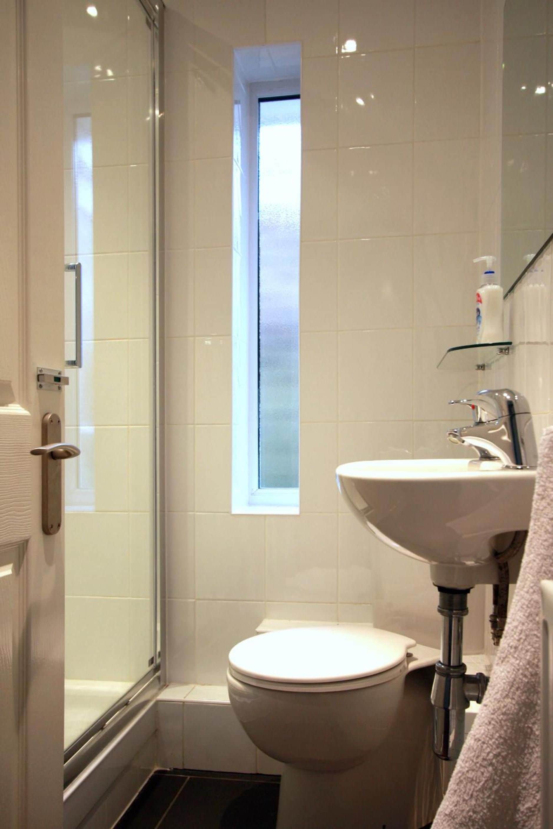 Un baño con cabina de ducha de vidrio, inodoro y lavamanos, con una toalla colgada en la pared.