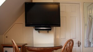 Una habitación con una televisión de pantalla plana en la pared, sobre una mesa y sillas de madera.