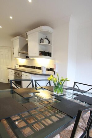 A modern kitchen with white cabinetry, a glass dining table, and a vase with flowers. - Abacus Bed and Breakfast (Camberley)