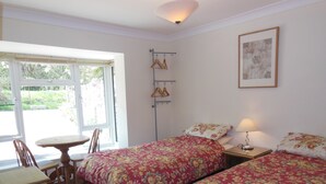 Una habitación con dos camas, una mesa, sillas, una lámpara y una ventana con vistas a zonas verdes.