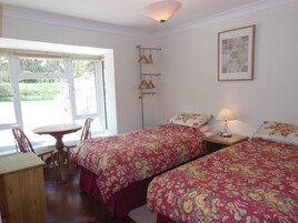 Una habitación con dos camas, una mesa, sillas, una lámpara y una ventana con vistas a zonas verdes.