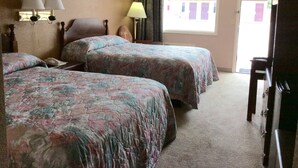 A hotel room with two beds, a desk, a lamp, and a door leading outside. - Budget Inn (Calhoun)