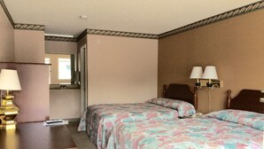 A hotel room with two beds, a desk, a lamp, and a mirror. - Budget Inn (Calhoun)