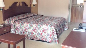 A hotel room with a bed, a desk, a chair, and a small table. - Budget Inn (Calhoun)
