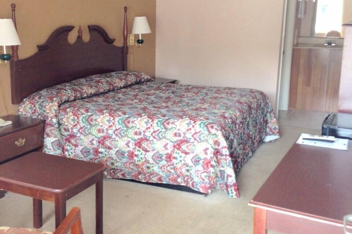 Quarto de hotel com uma cama, uma mesa, uma cadeira e uma mesinha.