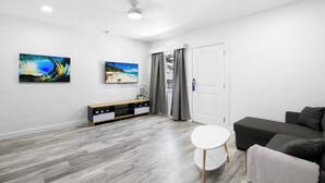 Ein modernes Wohnzimmer mit einem grauen Sofa, einem weißen runden Tisch und einem Fernseher an der Wand.