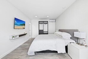 Une chambre à coucher moderne avec un lit, une table de chevet avec une lampe, un téléviseur fixé au mur et une armoire avec un miroir.