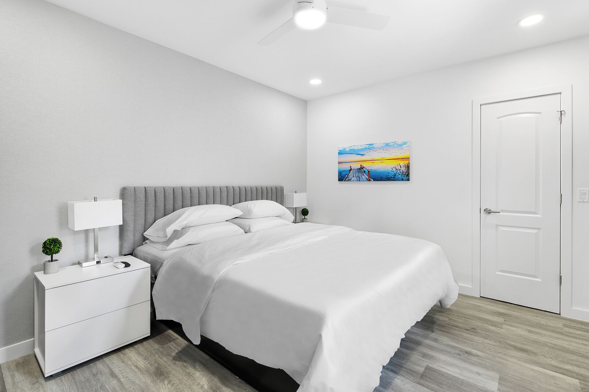 A bedroom with a bed, nightstand, lamp, and a painting on the wall.