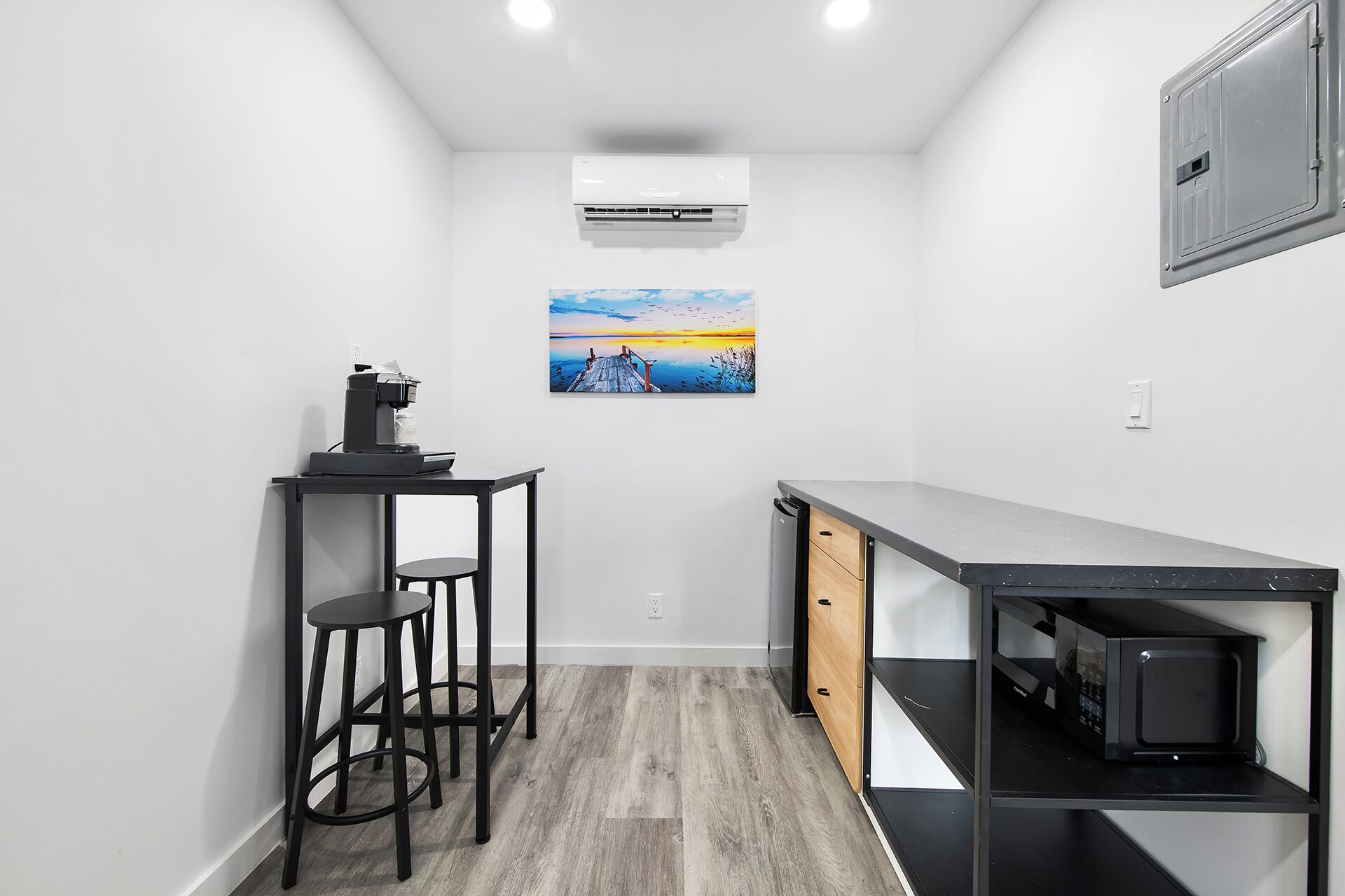 Una kitchenette compacta con cafetera, un pequeño comedor con taburetes y un microondas.