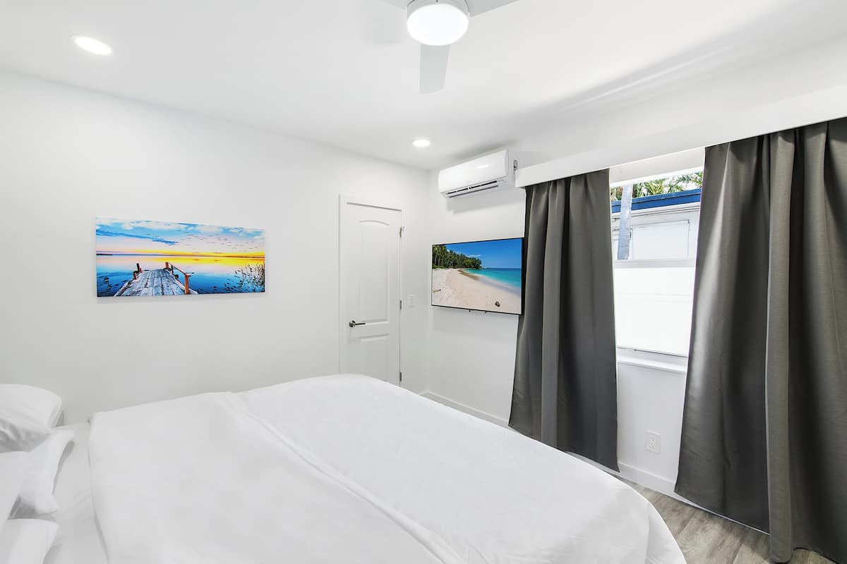 Habitación de hotel con cama, un cuadro de un atardecer, televisor y aire acondicionado.