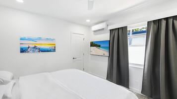 Habitación de hotel con cama, un cuadro de un atardecer, televisor y aire acondicionado.