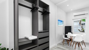 Ein modernes Zimmer mit einem grauen Kleiderschrank, einem kleinen Tisch mit weißen Stühlen und einem Bild an der Wand.