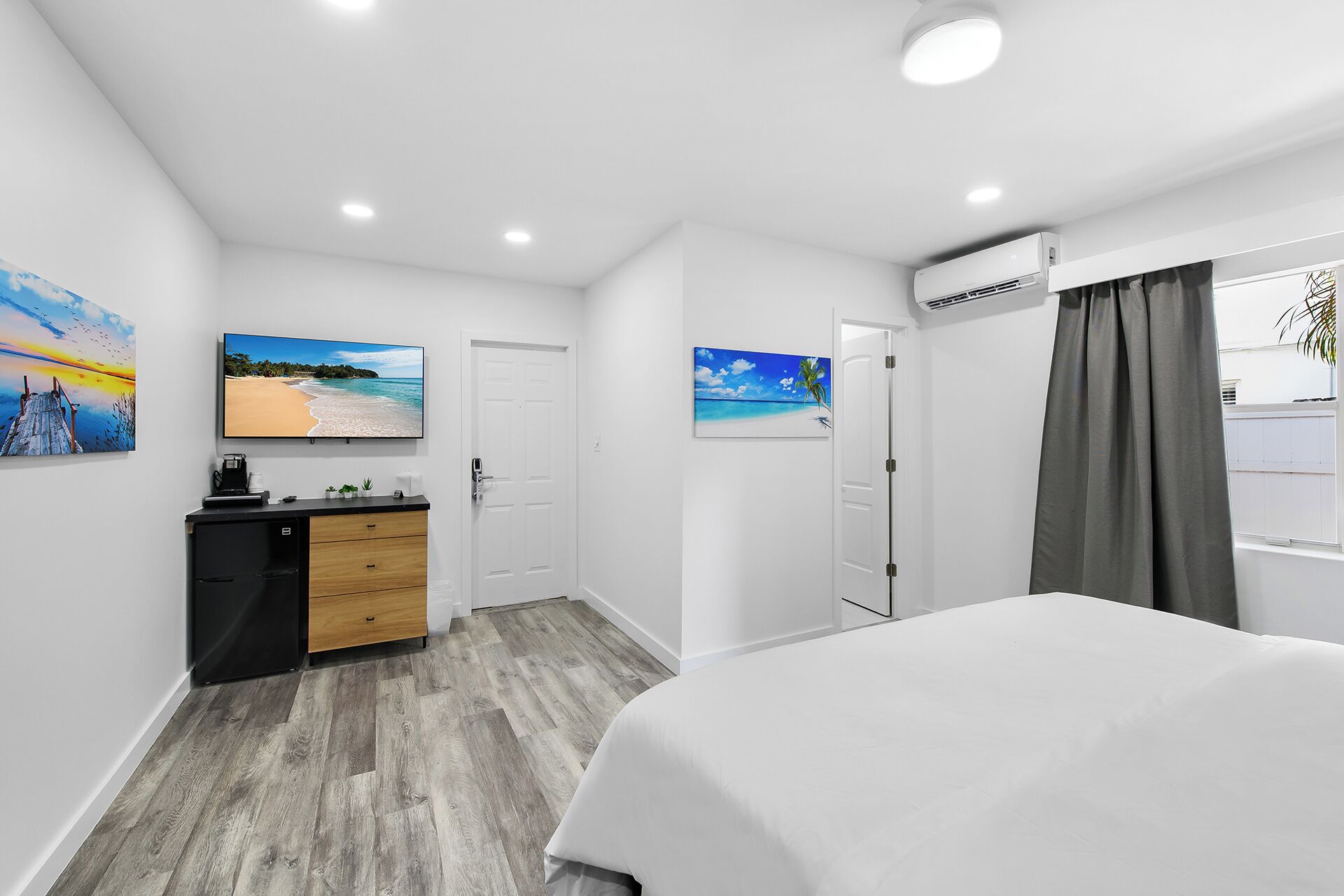 A modern hotel room with a bed, a desk with a computer, and artwork on the walls.