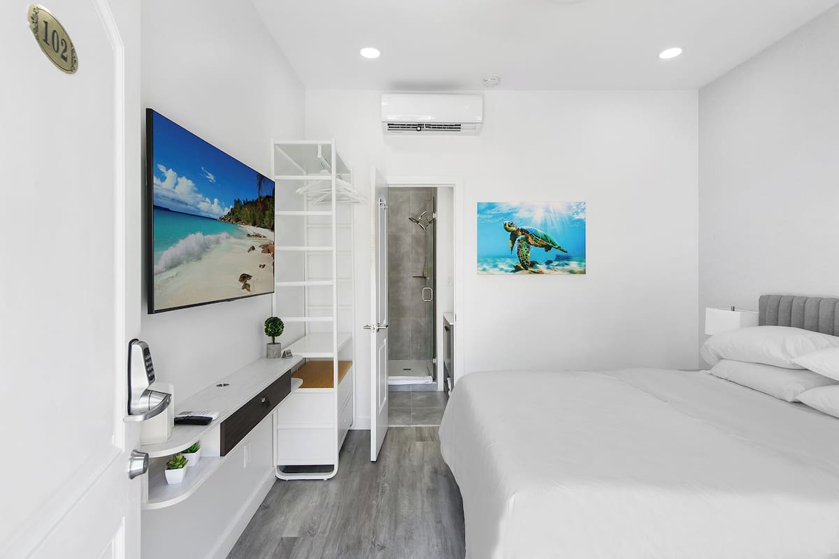 Un dormitorio moderno con cama, ducha, tocador con espejo y dos obras de arte en la pared.