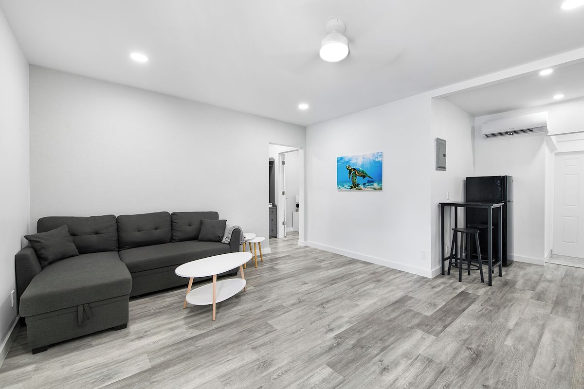 Una sala de estar moderna con un sofá seccional gris, una mesita blanca y un mueble de TV negro.