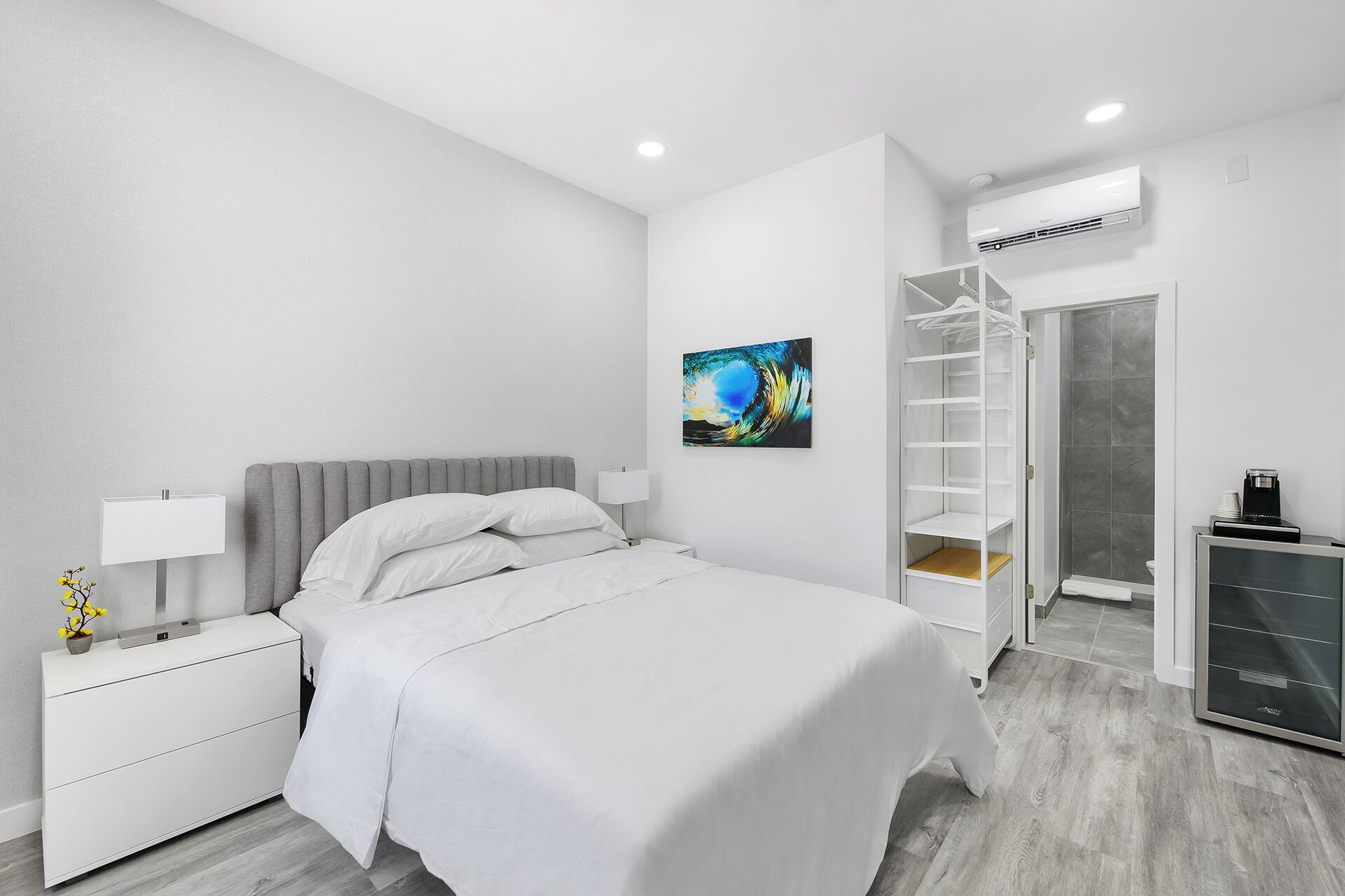 Ein modernes Hotelzimmer mit einem Bett, einem Nachttisch mit Lampe, einer Wand-Klimaanlage und einer Dusche.