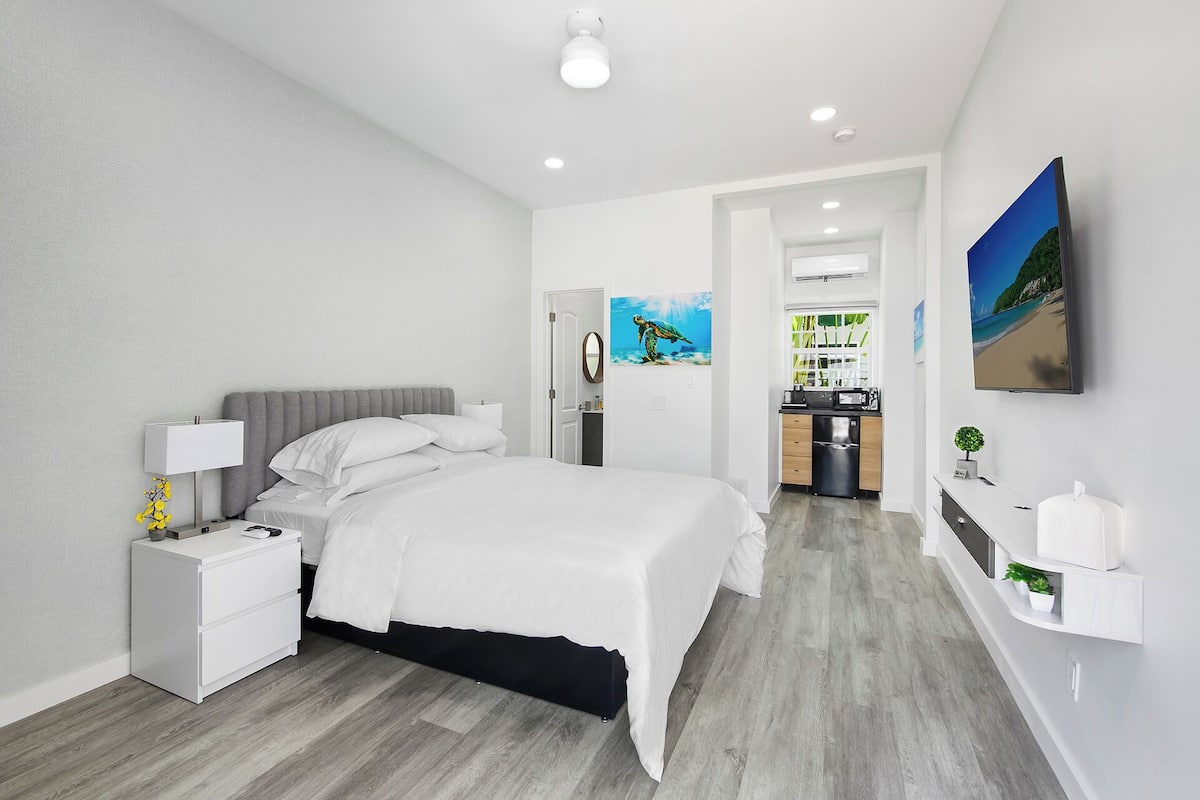 Una habitación de hotel moderna con una cama, mesita de noche, lámpara y vistas a la cocina y al baño.