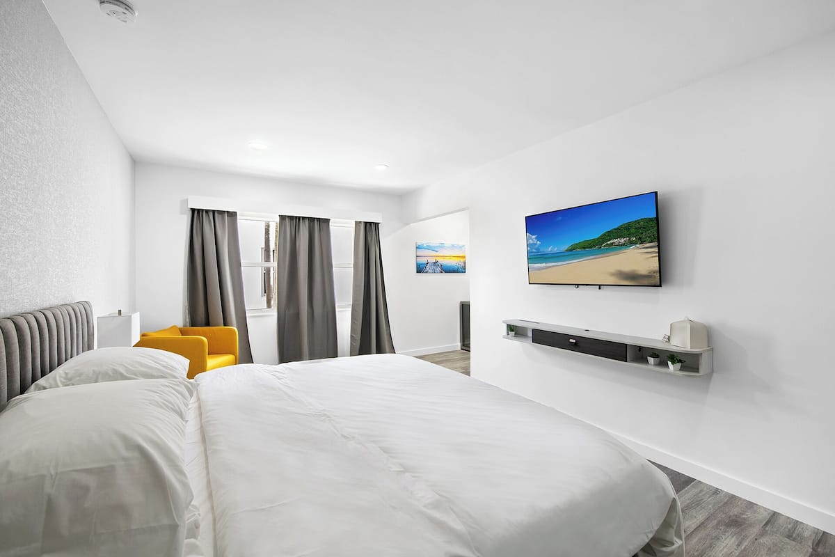 Una habitación de hotel moderna con una cama grande, un televisor montado en la pared y un estante pequeño con una planta.