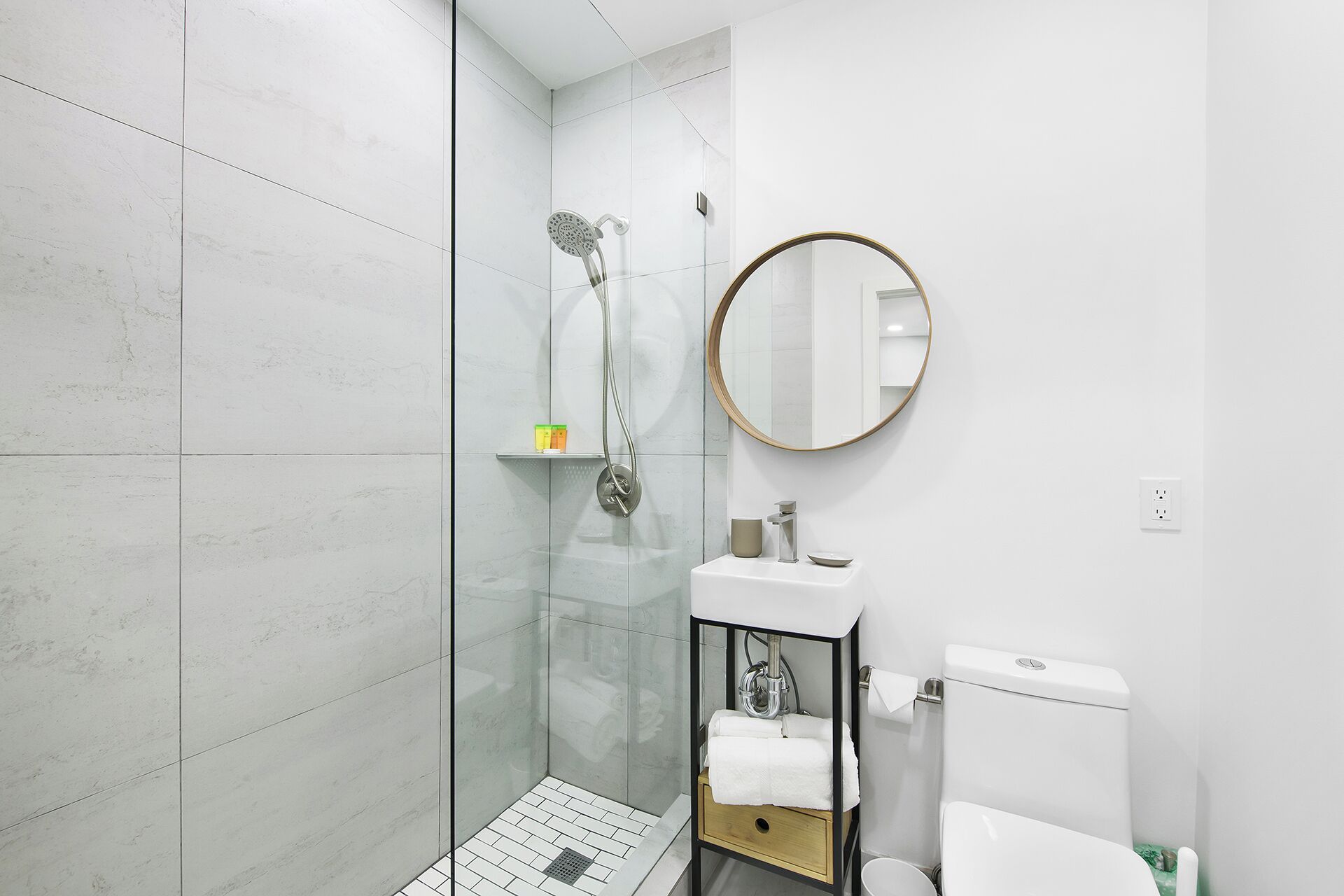 A modern bathroom with a glass shower enclosure, a round mirror, a white sink, and a toilet.