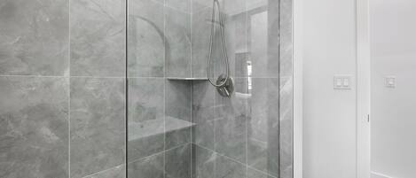 A modern bathroom with a glass-enclosed shower, grey marble tiles, and a white door.
