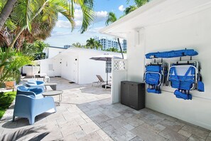 Un espace patio avec des sièges d’extérieur, un mur blanc orné de sacs bleus et, en arrière-plan, une vue sur des bâtiments.