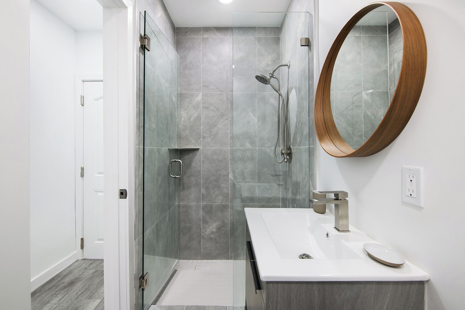 A modern bathroom with a glass-enclosed shower, a white sink, and a wooden-framed mirror.