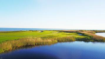 Un campo de golf con una masa de agua en primer plano y una vista despejada del océano al fondo.