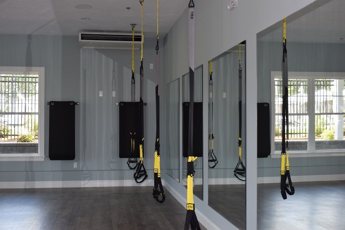 Une salle dotée de grands miroirs, de sangles de suspension TRX et d’un tapis de sport noir.