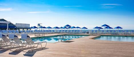 A poolside area with sun loungers and umbrellas, a wooden deck, and a view of the ocean.
