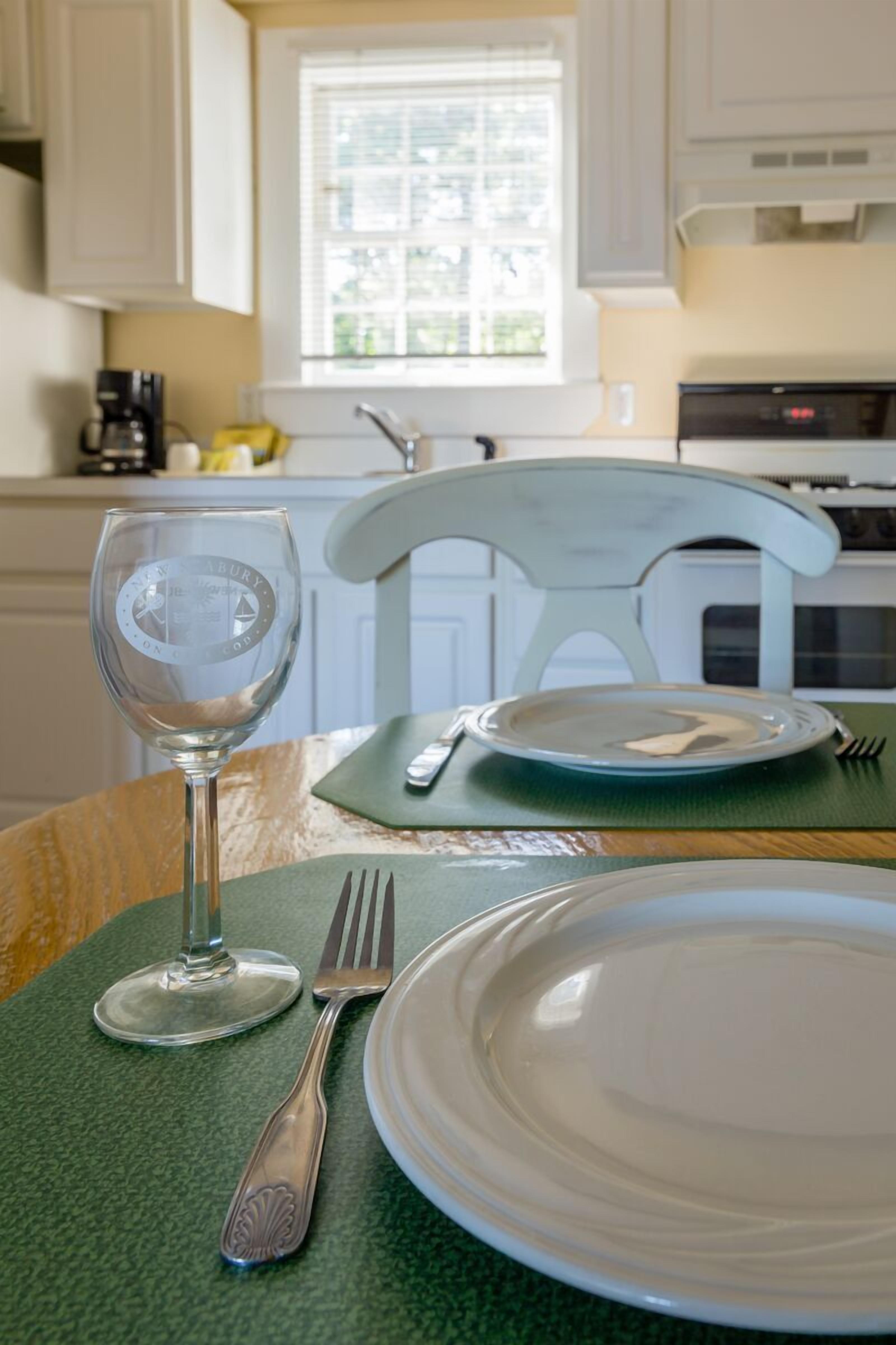 A dining table with a green placemat, a white plate, a fork, and a wine glass.