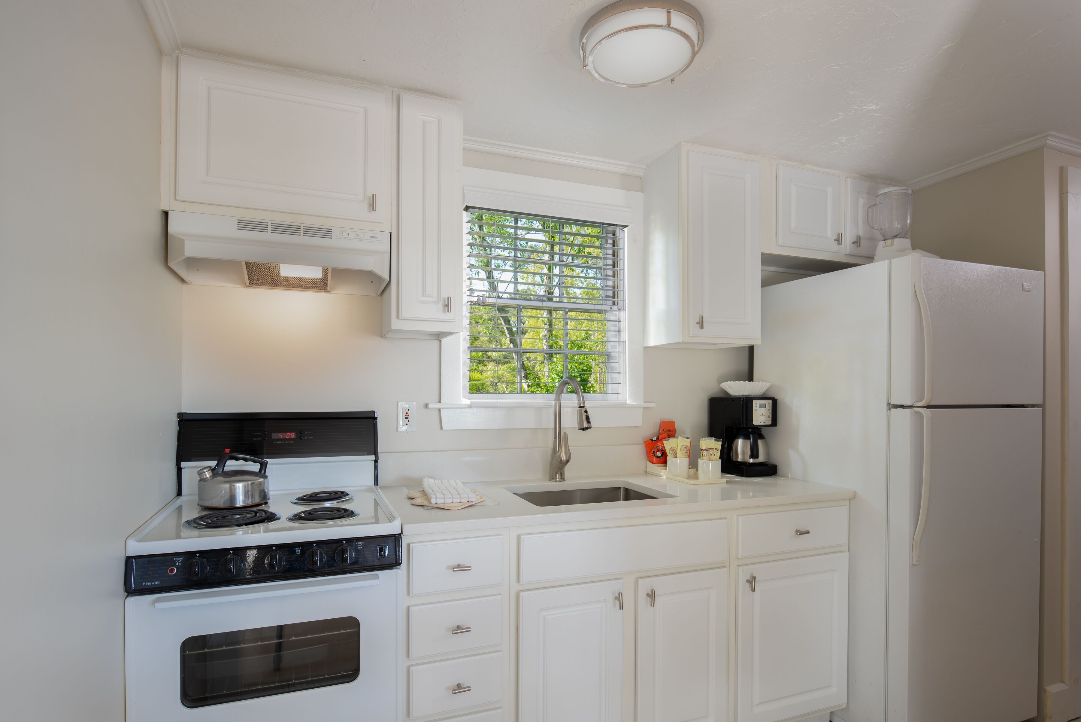 A compact kitchen with white cabinets, a stove, a sink, and a refrigerator.