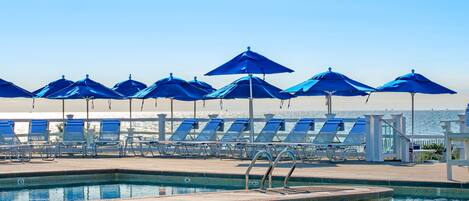 A pool area with blue umbrellas and sun loungers.