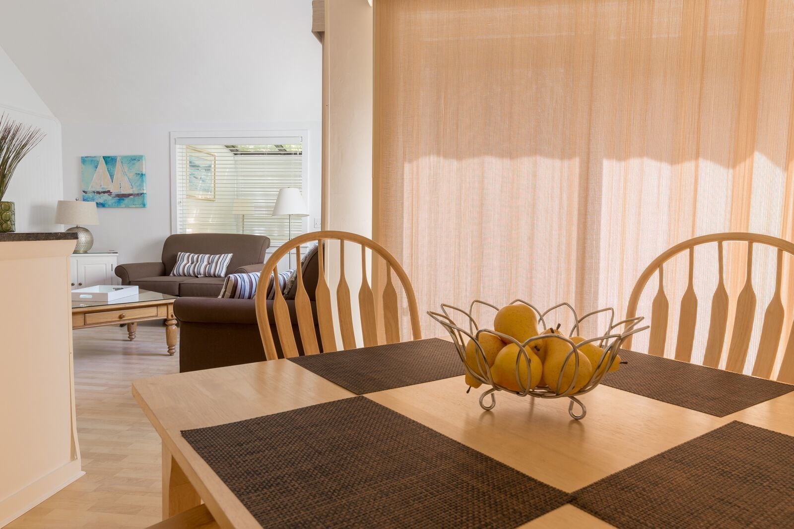 A dining area with a wooden table, two chairs, and a fruit bowl.