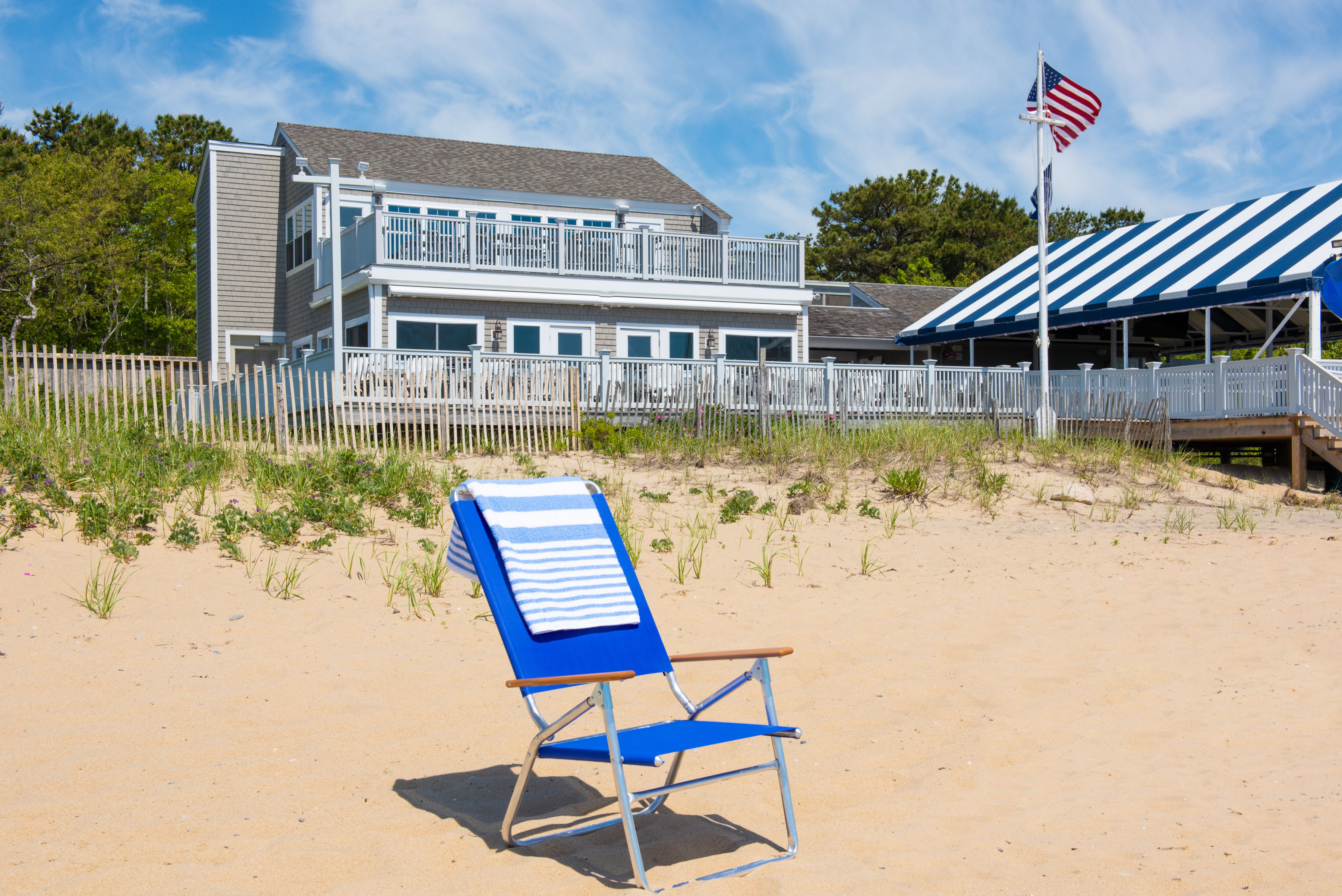 A beach house with a balcony, a flag, and a beach chair.