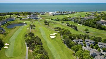 Un parcours de golf avec un grand plan d’eau en arrière-plan, entouré de zones résidentielles.