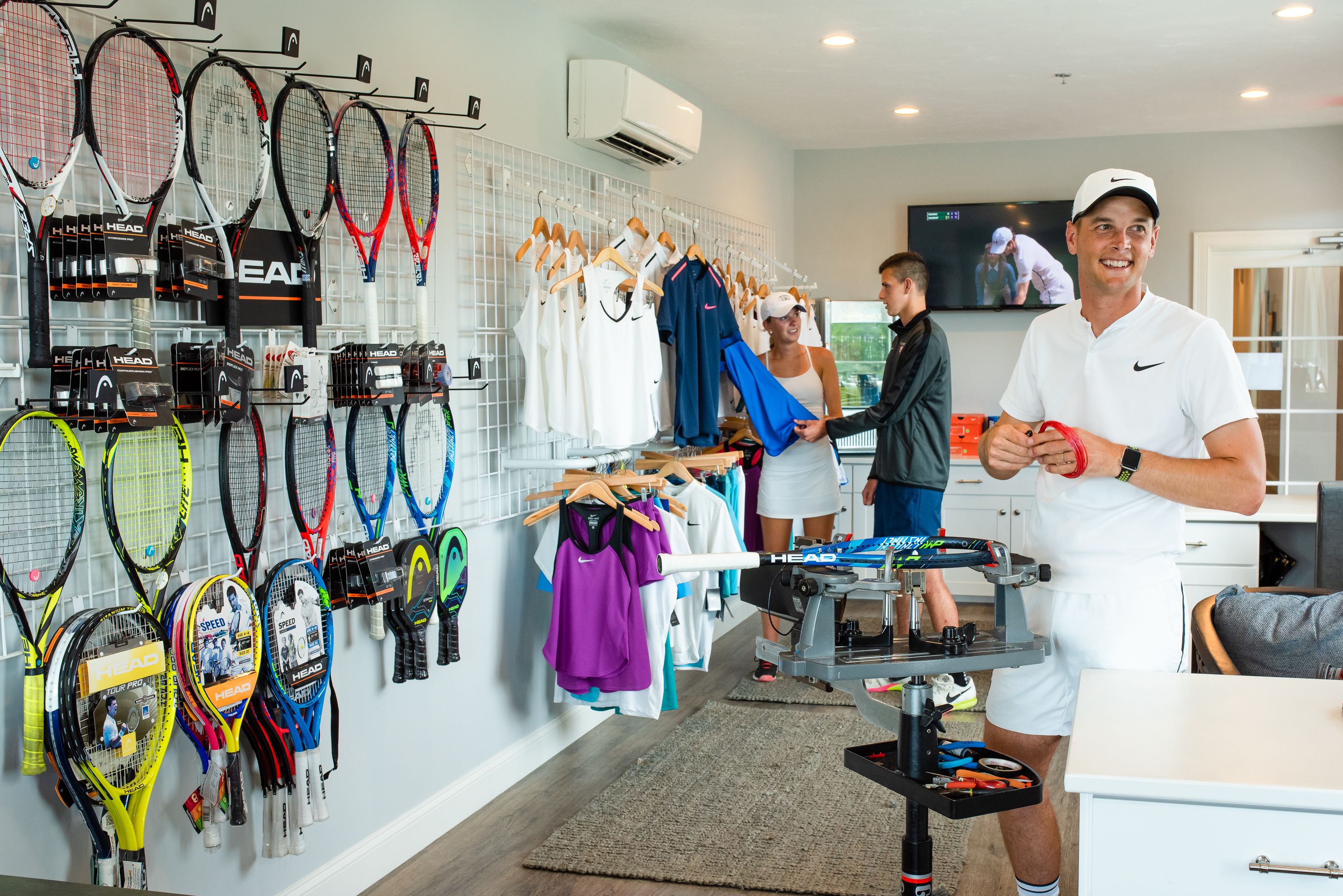 Exhibición de raquetas de tenis con diferentes modelos y un perchero con ropa deportiva.