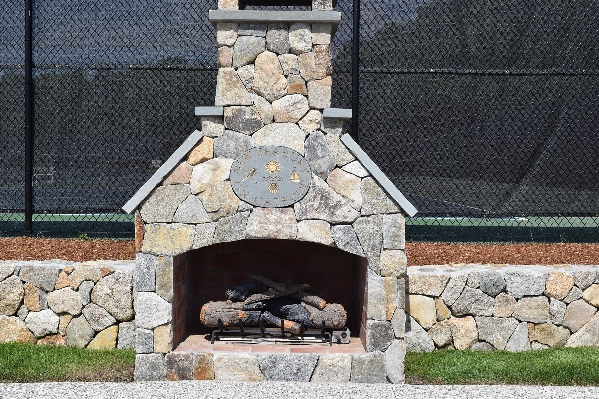 A stone fireplace with logs, surrounded by a stone wall and a metal fence.