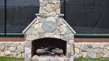 A stone fireplace with logs, surrounded by a stone wall and a metal fence.