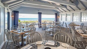 Un restaurant dont les tables sont dressées pour le service, avec vue sur une plage.