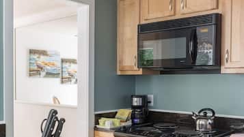 A kitchen with wooden cabinets, a black microwave, a kettle, and two white mugs on the counter.