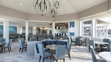 A spacious dining area with multiple tables and chairs, a bar area with a counter, and a large window offering a view of the outside.
