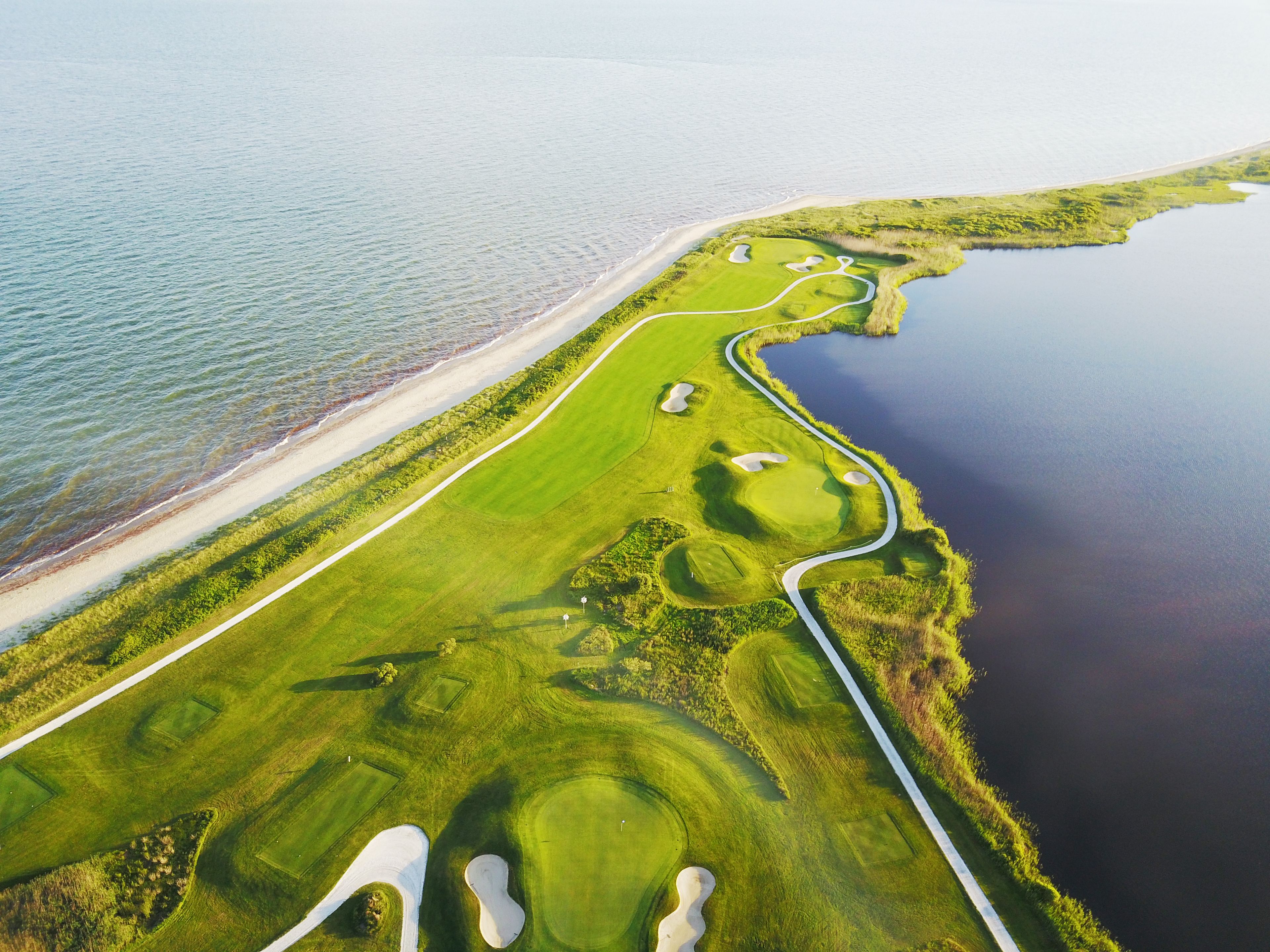 An aerial view of a golf course with sand bunkers, a water body, and a beach.