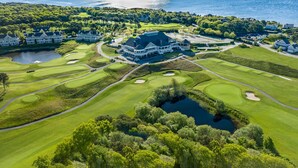 Un parcours de golf doté d’un club-house, d’un lac et entouré d’arbres.