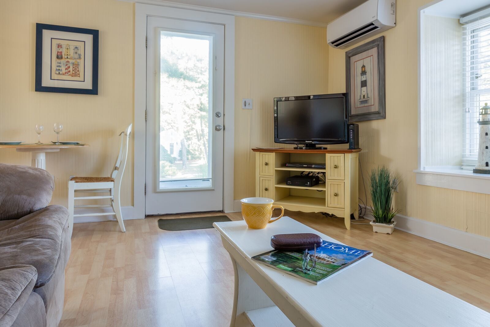 A cozy living room with a sofa, a coffee table with a magazine, a television on a stand, and a door leading outside.