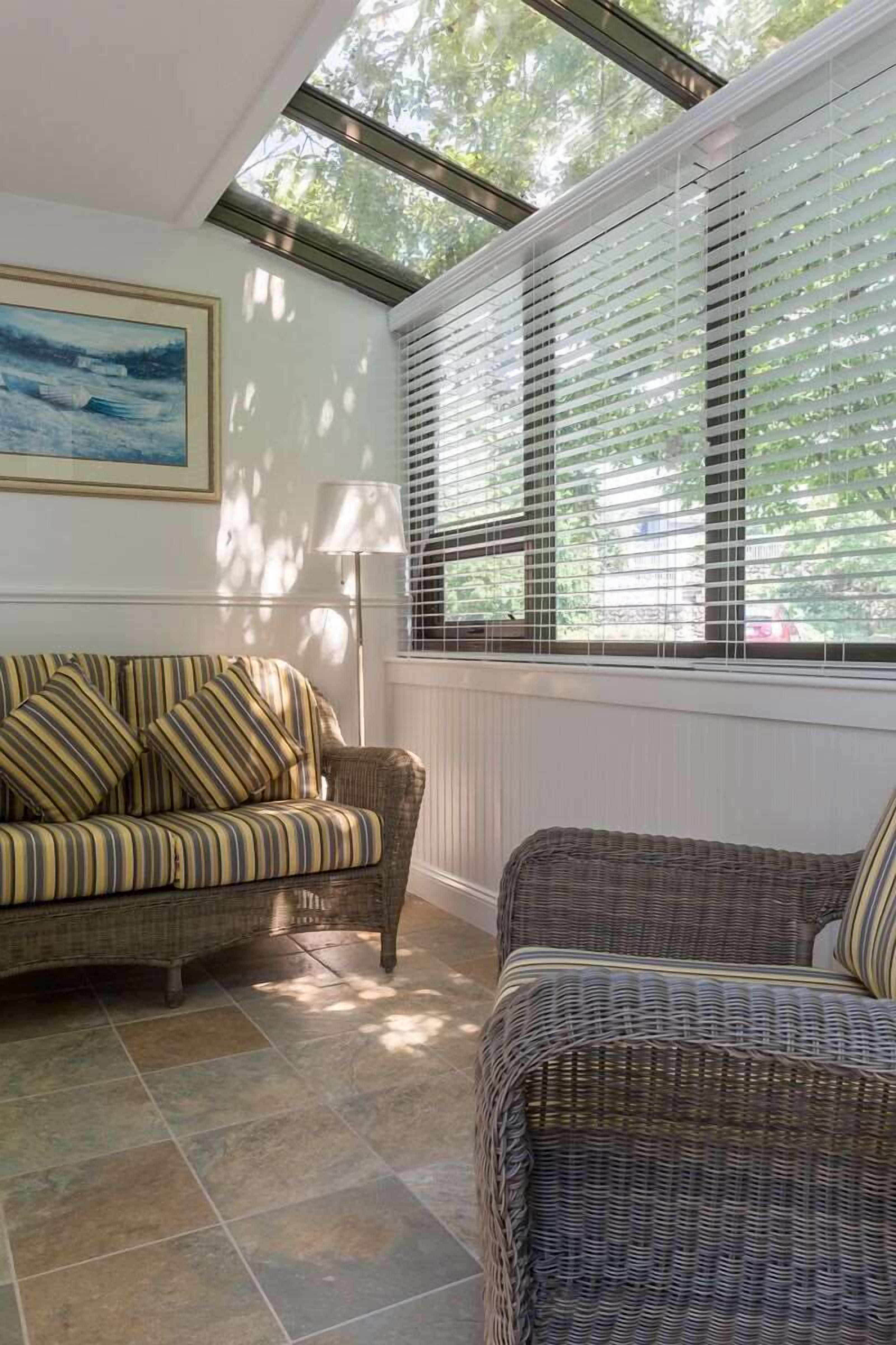 Una habitación iluminada por el sol con un sofá a rayas, un sillón de mimbre y una lámpara.
