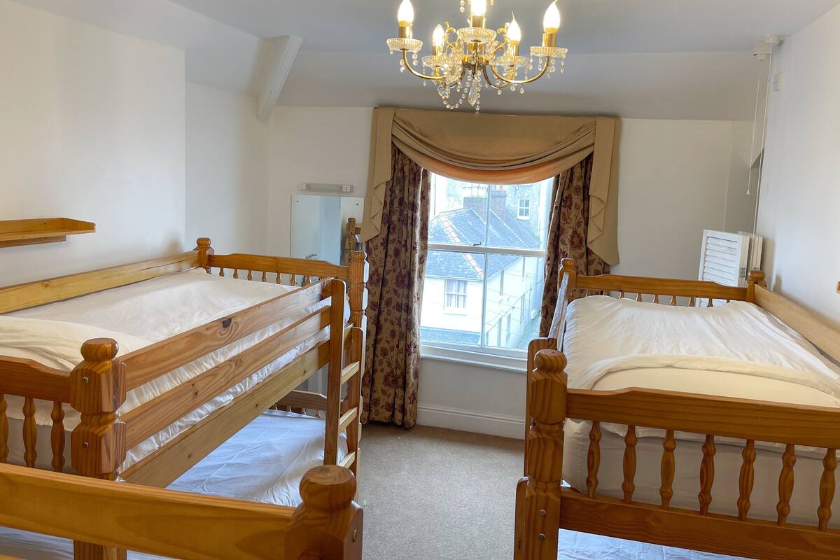 A room with two wooden bunk beds, a chandelier, a window with curtains, and a radiator.