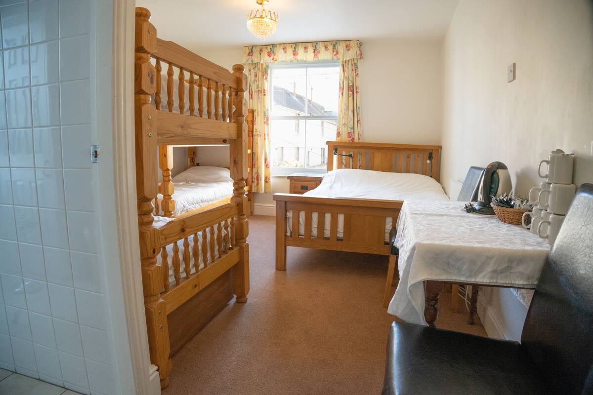 A room with two wooden beds, a table with a white tablecloth, and a coffee station.