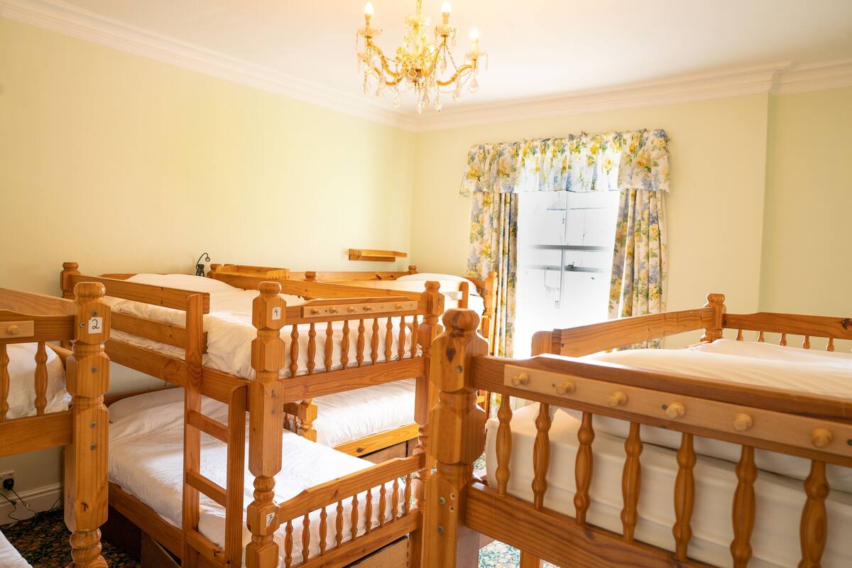 A room with bunk beds, a chandelier, and a window with floral curtains.